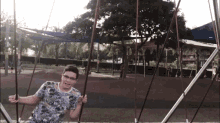a boy wearing glasses is sitting on a swing at a park