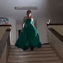 a woman in a long green dress is walking down stairs