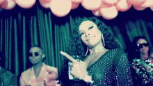 a woman in a polka dot dress is pointing at the camera while dancing in front of balloons .