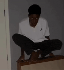 a young man wearing a white adidas shirt squatting on a table