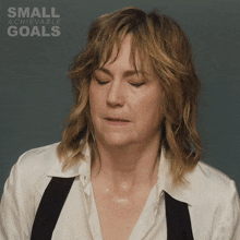 a woman in a white shirt and black suspenders has her eyes closed and the words small achievable goals behind her