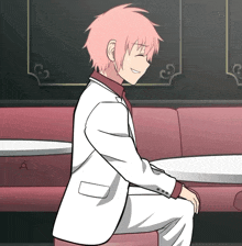 a man in a white suit sits on a red couch smiling