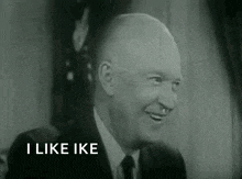 a man in a suit and tie is smiling and says `` i like ike '' in a black and white photo .