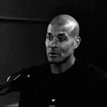 a man in a black shirt stands in front of a microphone with a t on his shirt