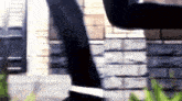 a person is standing in front of a brick wall wearing black pants and black shoes .