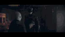 a man in a batman costume is fighting another man in a dark room with a sword .