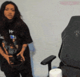 a woman wearing a t-shirt that says " ht " stands in front of a chair
