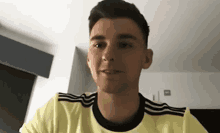 a young man wearing a yellow adidas shirt is sitting in a room and smiling .