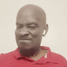 a bald man wearing a red shirt and ear buds makes a funny face