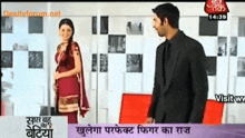 a man in a suit stands next to a woman in a red dress on a tv screen
