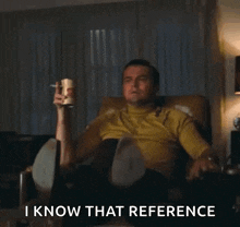 a man is sitting in a chair pointing at something with the words " i know that reference " above him