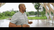 a man in a grey shirt with a tattoo on his arm stands in a park