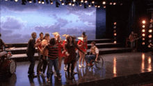 a group of people are dancing on a stage and one of them is in a wheelchair