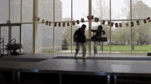 two people are dancing on a stage in front of a window with flags hanging from the ceiling