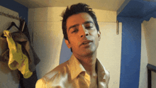 a man in a gold shirt is standing in front of a blue wall