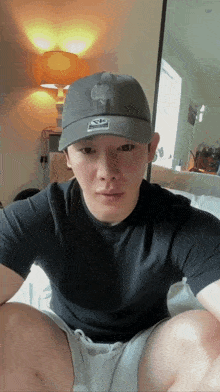 a man wearing a champion hat sits on a bed in front of a mirror