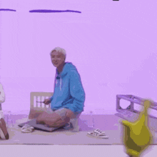 a man in a blue hoodie is kneeling down on the floor holding a yellow umbrella .