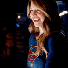 a woman in a superman costume is smiling and looking at the camera in a dark room .
