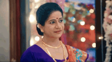 a woman wearing a purple top and a gold necklace is standing in front of a window .