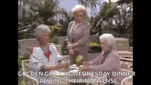 three older women are sitting at a table talking to each other while holding hands .