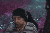 a man wearing headphones and a striped shirt is sitting in a chair in front of a purple background .