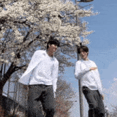 two men standing next to each other in front of a tree with flowers