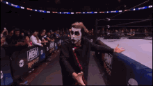 a man in a mask stands in front of a wrestling ring that has aew written on it