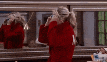 a woman in a red robe is looking at herself in a mirror .