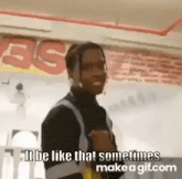 a man is standing in a room with a sign on the wall that says `` it be like that sometimes '' .