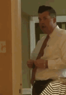 a man in a white shirt and red tie adjusts his tie in front of a mirror