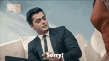 a man in a suit and tie is sitting on a couch and says sorry