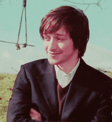 a man in a suit is smiling with his arms crossed in a field