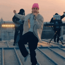 a man in a pink beanie is singing into a microphone on a rooftop