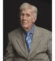 an elderly man wearing a suit and tie looks at the camera