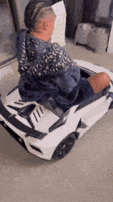 a man in a blue louis vuitton jacket sits in a toy car