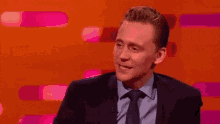 a man in a suit and tie is sitting in front of a pink background and says yep .