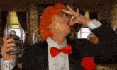 a woman in a tuxedo and red bow tie is drinking from a glass