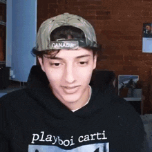 a young man wearing a hat and a playboi carti hoodie is looking at the camera .