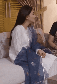a woman in a white dress sits on a couch with a blue scarf around her waist