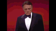 a man in a tuxedo and bow tie is singing .
