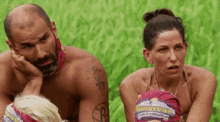 a man and a woman are sitting in the grass wearing survivor bandanas