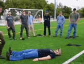 a group of men are standing around a man who is laying on the grass
