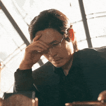 a man wearing glasses and a suit holds his hand to his head