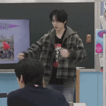 a man in a plaid jacket is standing in front of a blackboard with a picture of a rocket on it