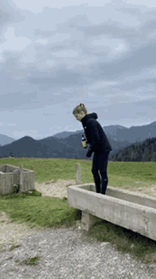 a young man is standing next to a trough in a field .