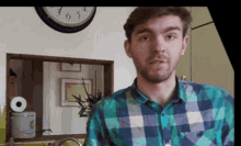 a man in a plaid shirt is standing in front of a clock that shows the time as 6:55