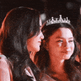 a woman wearing a tiara stands next to another woman wearing a tiara