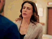 a woman in a plaid jacket talks to a man