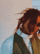 a woman 's hair is blowing in the wind while wearing a white shirt and a green vest