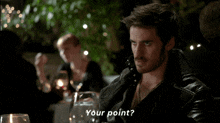 a man in a leather jacket is sitting at a table and asking " your point "